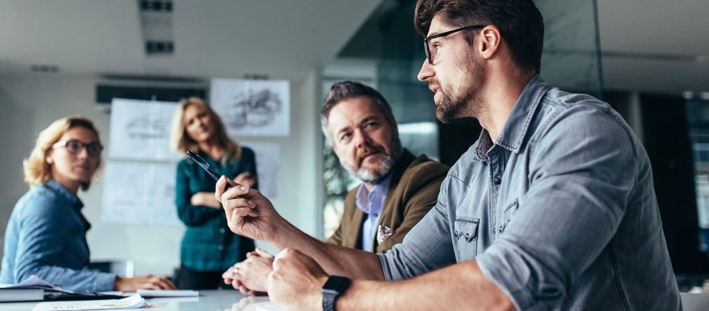 Young designer giving some new ideas about project to his partners in conference room. Business people discussing over new business project in office.